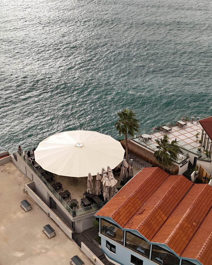 Deniz kıyısındaki çatı terasında açık yuvarlak şemsiye, havadan